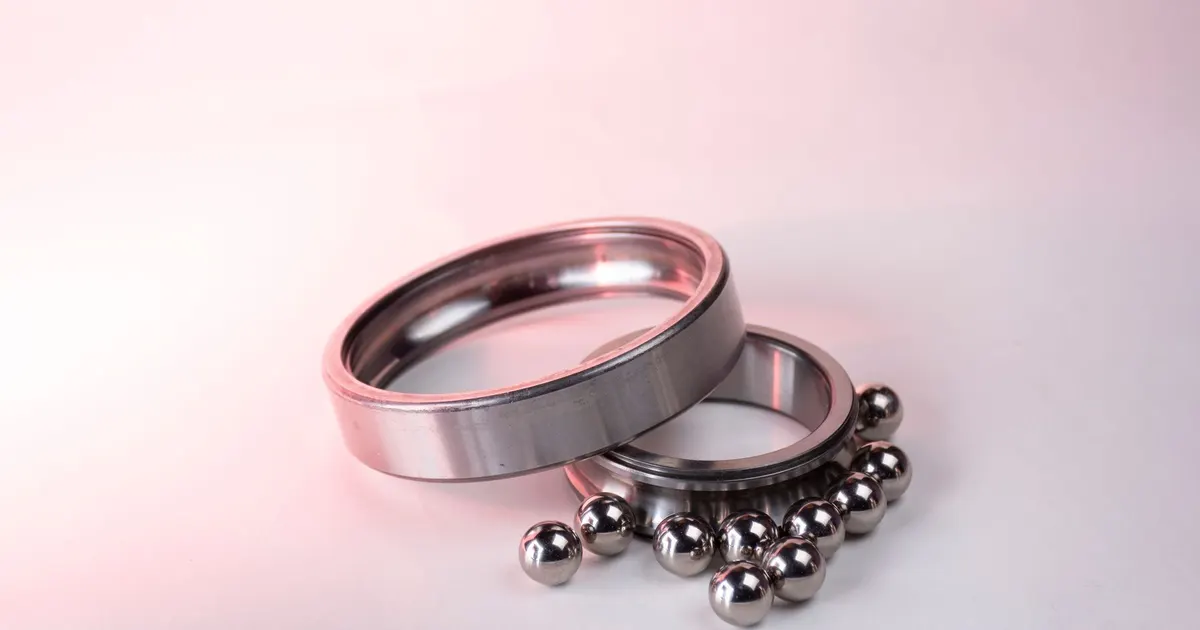Two steel bearing rings with loose balls on a pink background, showing the parts of a ball bearing used in bike hubs and headsets