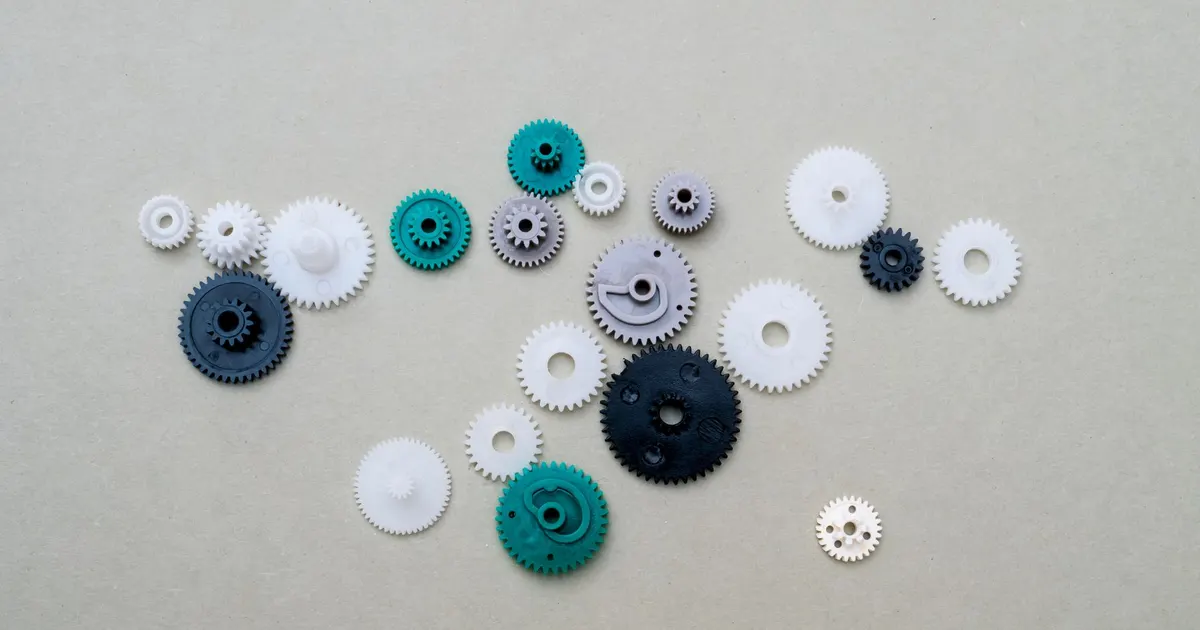 Small plastic gears in white, black and green on a flat gray surface