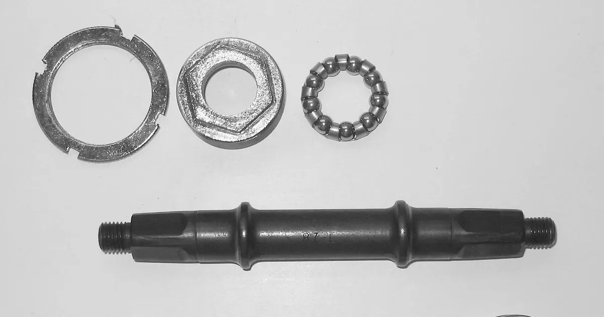 Cup and cone bicycle bottom bracket parts laid out on a white surface: spindle, lock ring, cones, cups and ball retainers