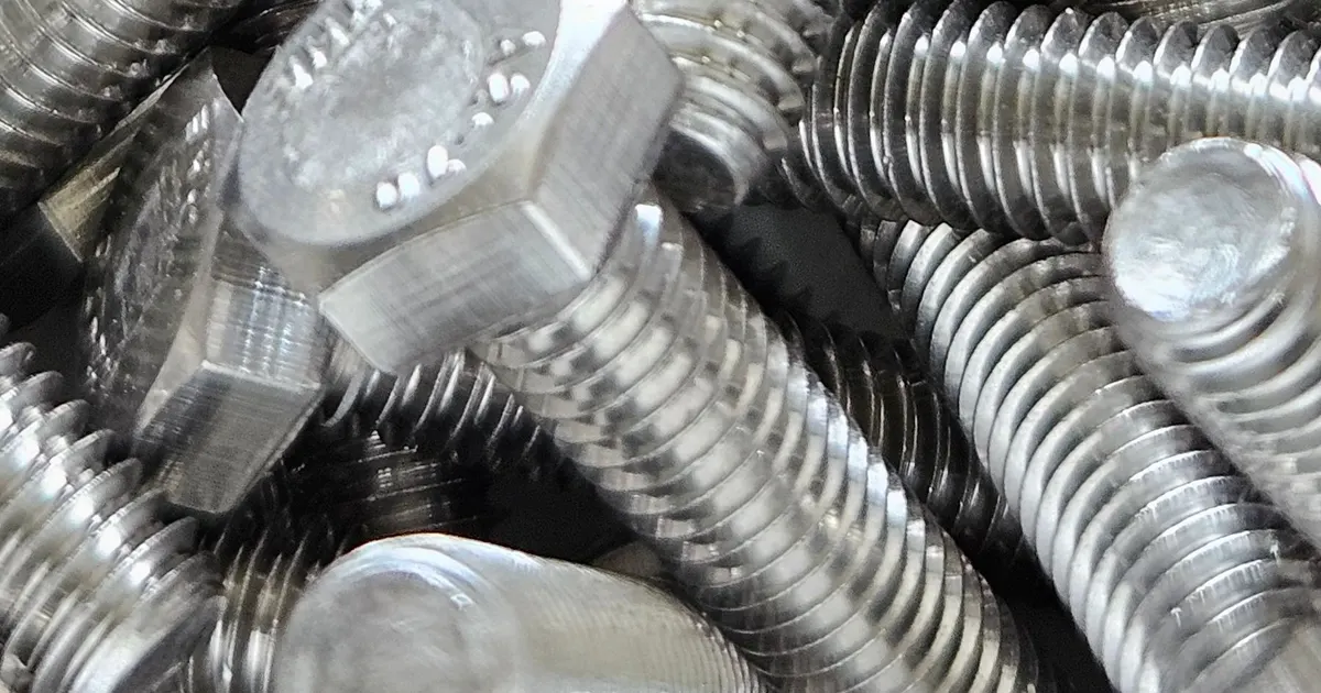 Pile of steel hex bolts and threaded studs with bright metallic finish